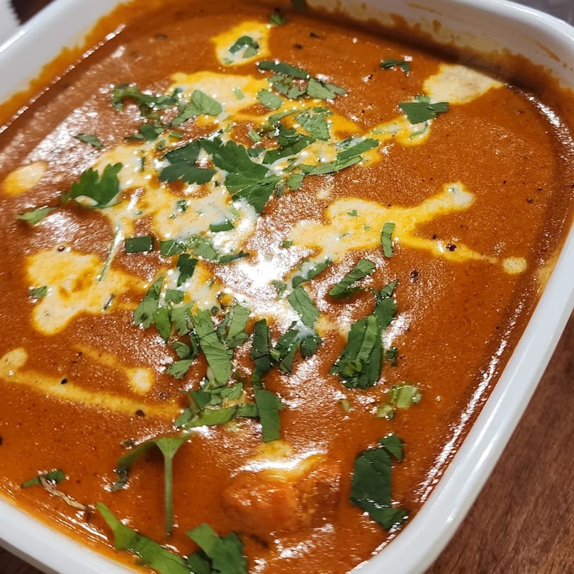 Close-up of Indian butter chicken, garnished with fresh cilantro and cream swirls in a white bowl.