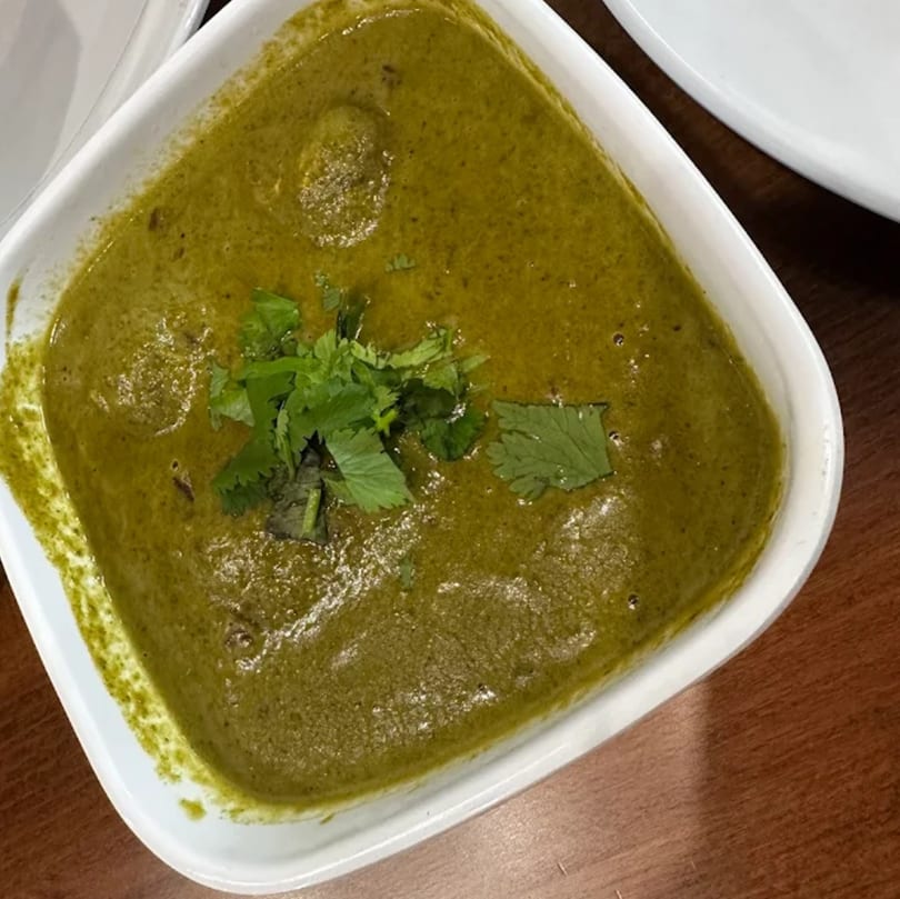 A close-up of a vibrant green Indian curry, garnished with fresh cilantro, in a white bowl.