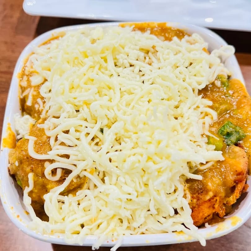 A close-up of an Indian dish from Aroma Indian Palace, topped with shredded white cheese.